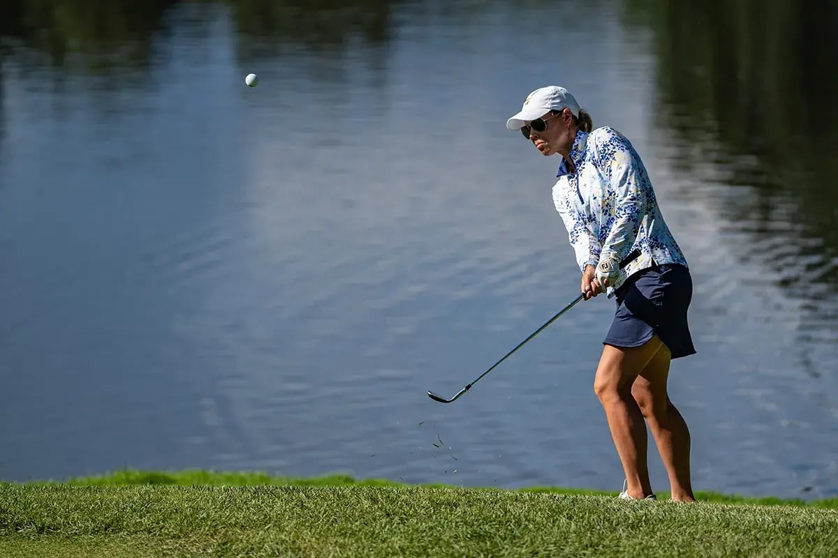 female golfer popping ball up away from water on slope