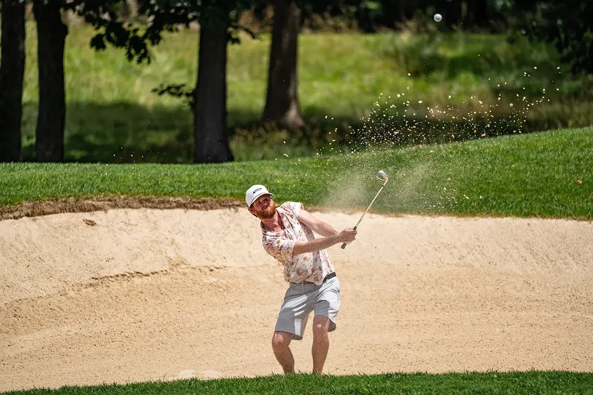 male golfer hitting ball sand splatters in foreground