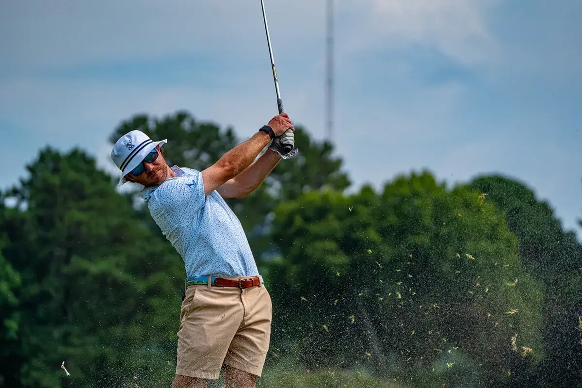 male golfer swings grass splatters in foreground