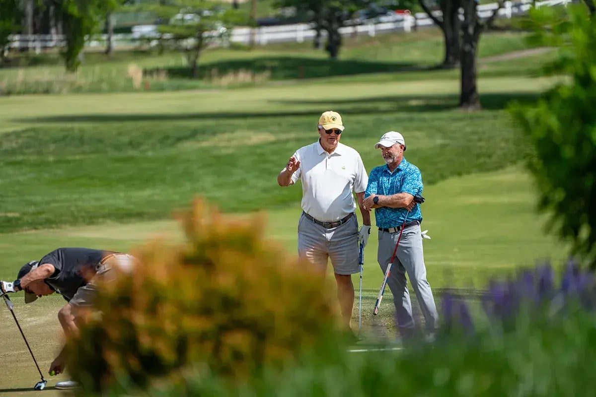 two male golfers discussing third golfer bending at hole