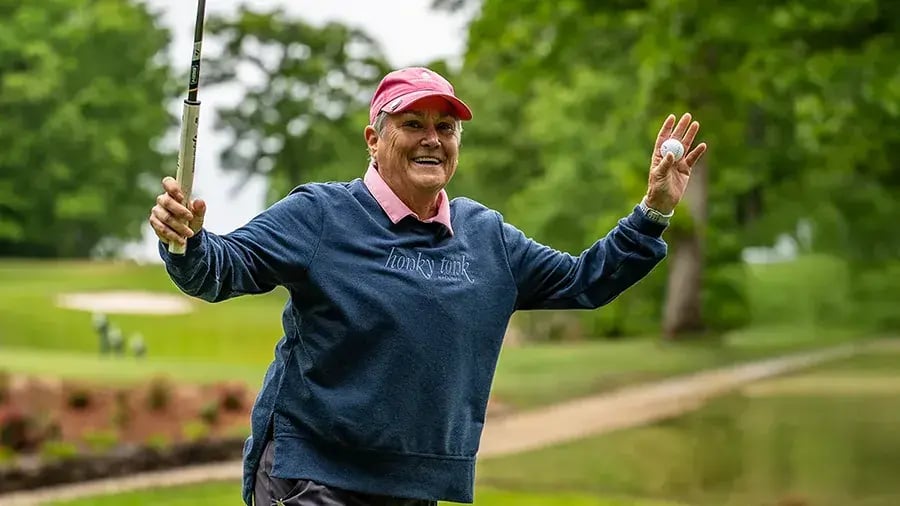 woman with golf ball in hand with arms raised