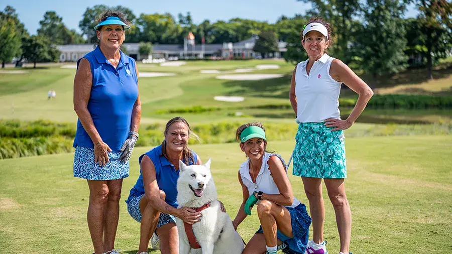 four female golfers posing with white dog